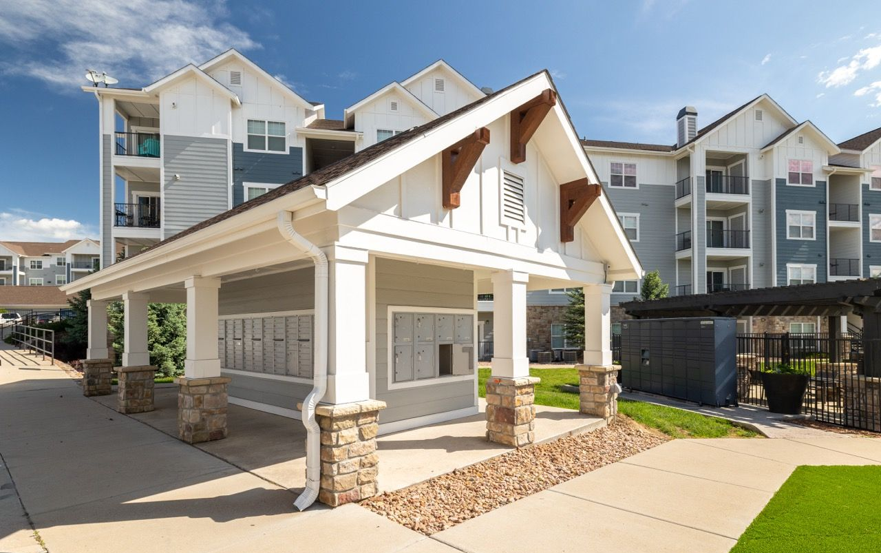 Exterior view of a modern apartment community with a covered mail area and multi-story buildings in the background.