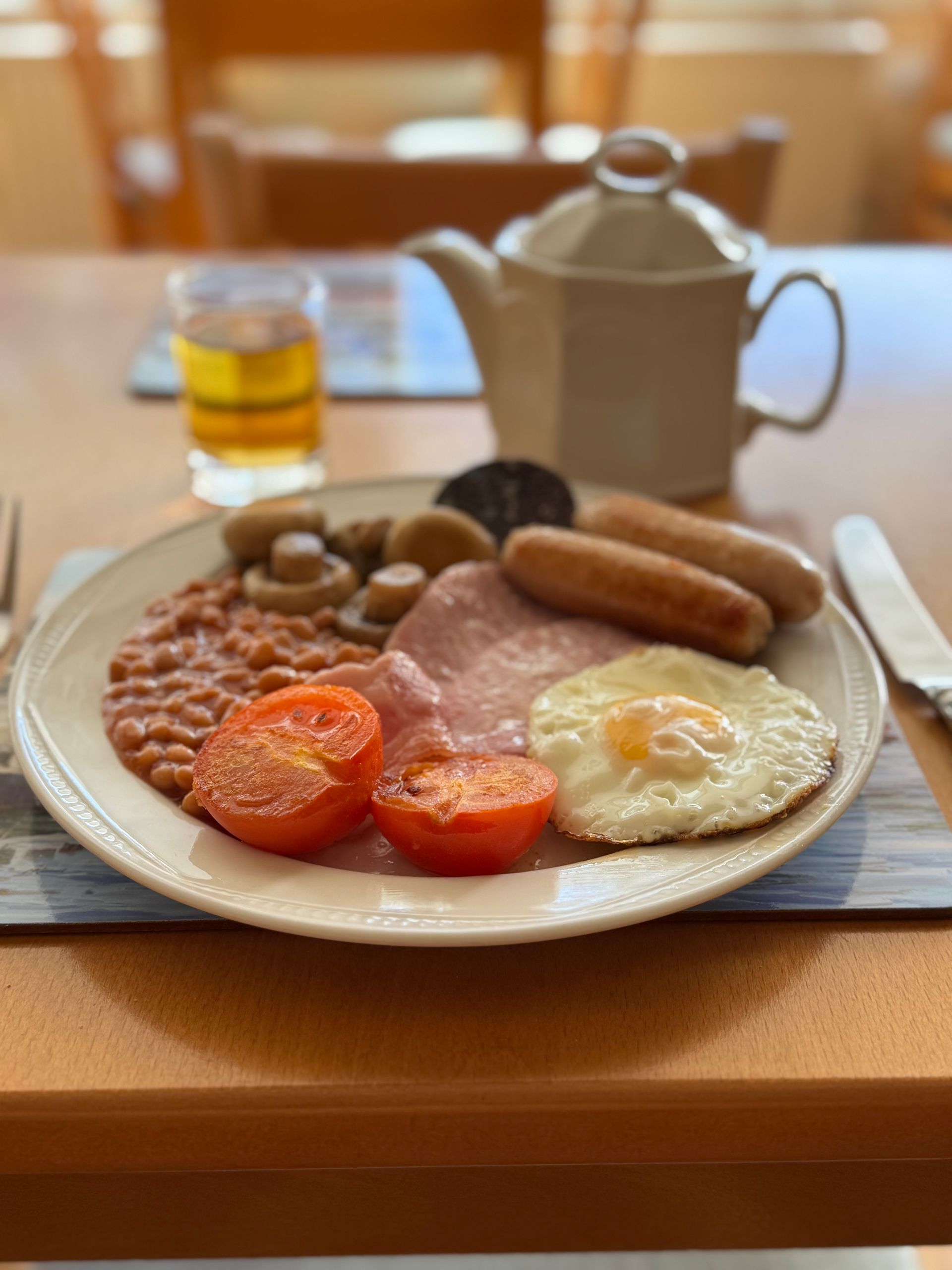 Full English breakfast: fried egg, sausages, ham, beans, mushrooms, tomatoes, black pudding, and tea.