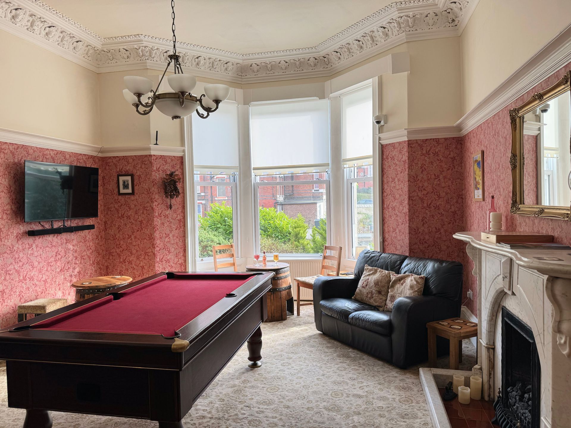 Pool table in a room with a sofa, fireplace, and window; red wallpaper, off-white trim.