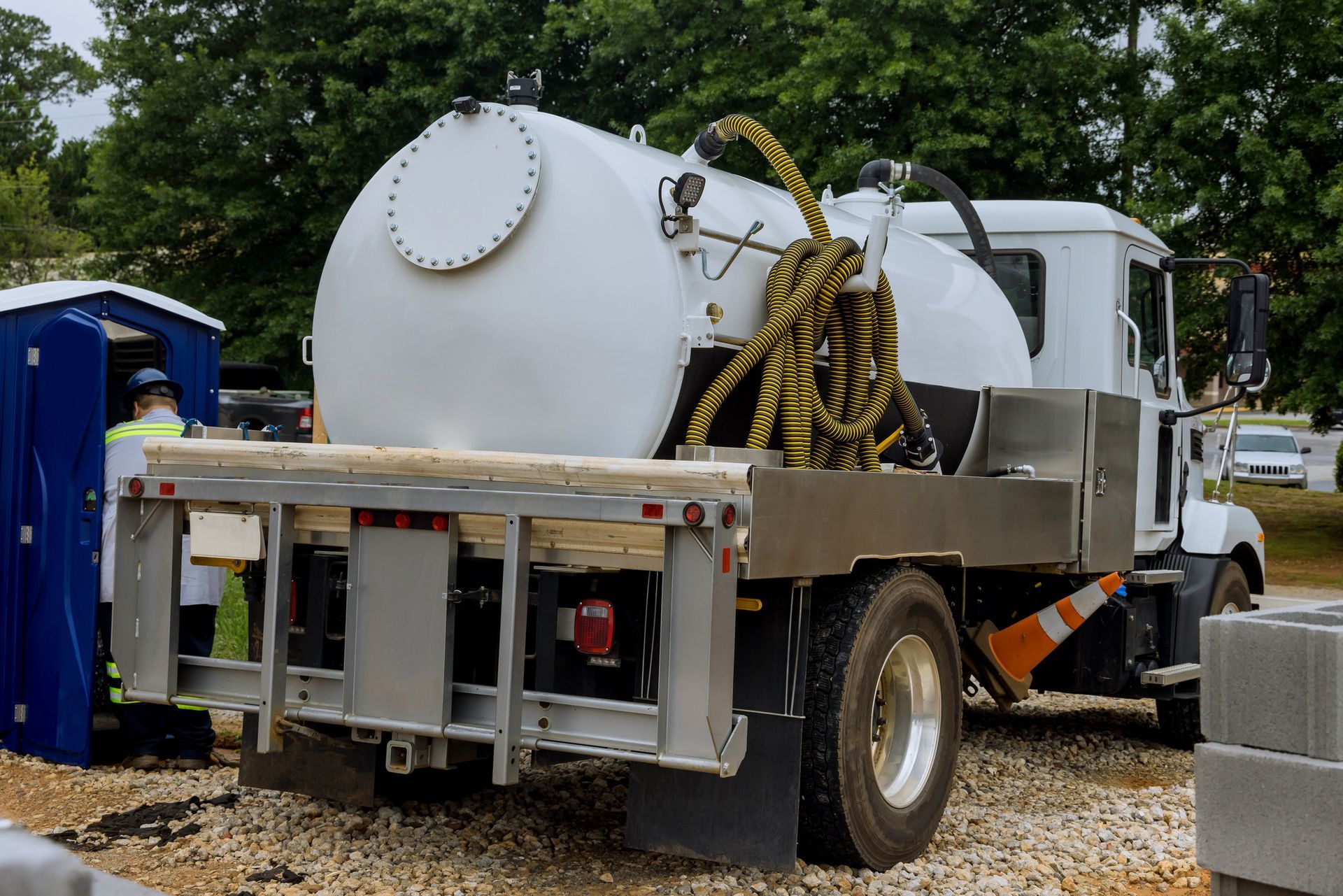 A white truck with a large tank on the back is parked in a gravel lot.