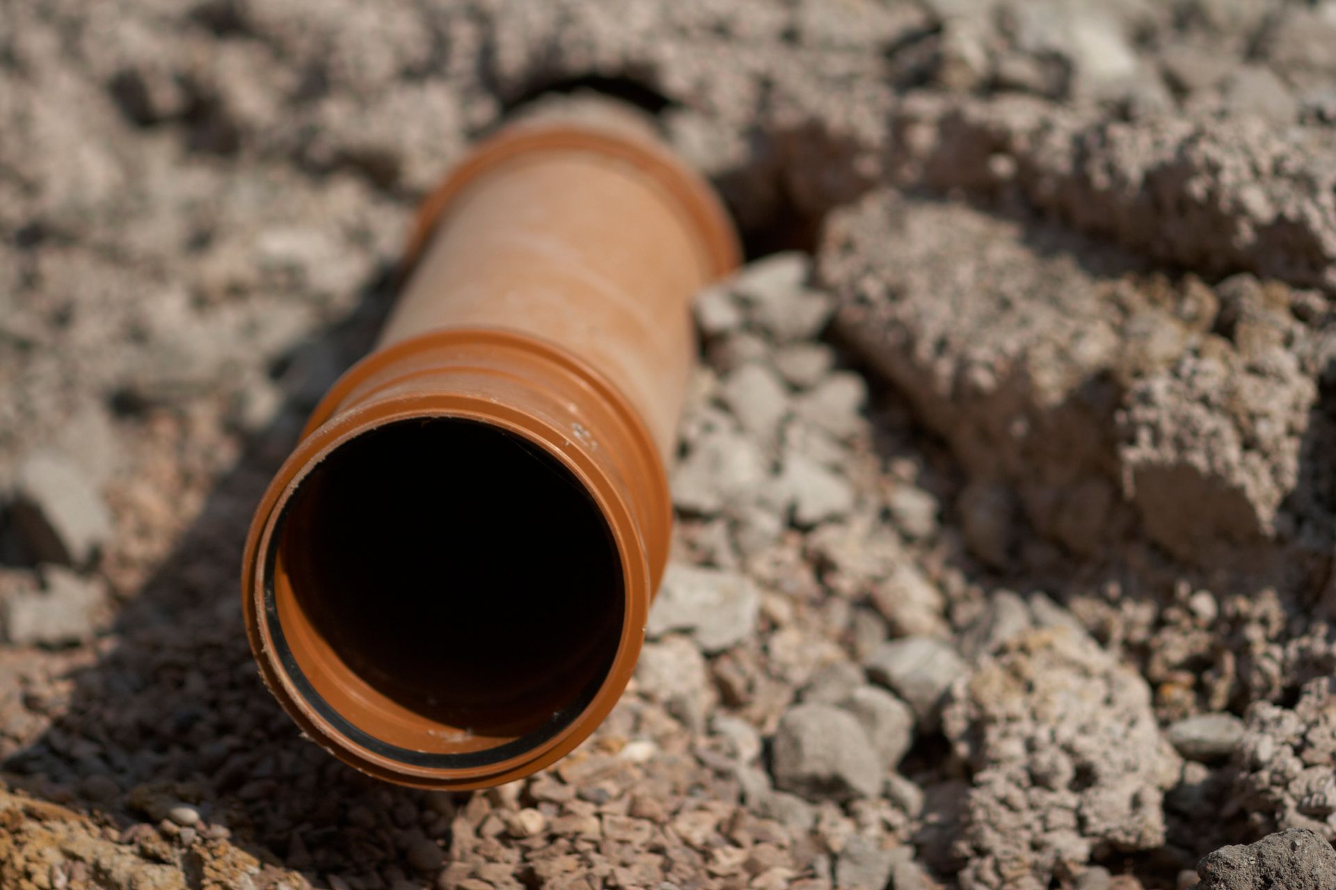 A brown pipe is laying on the ground in the dirt.