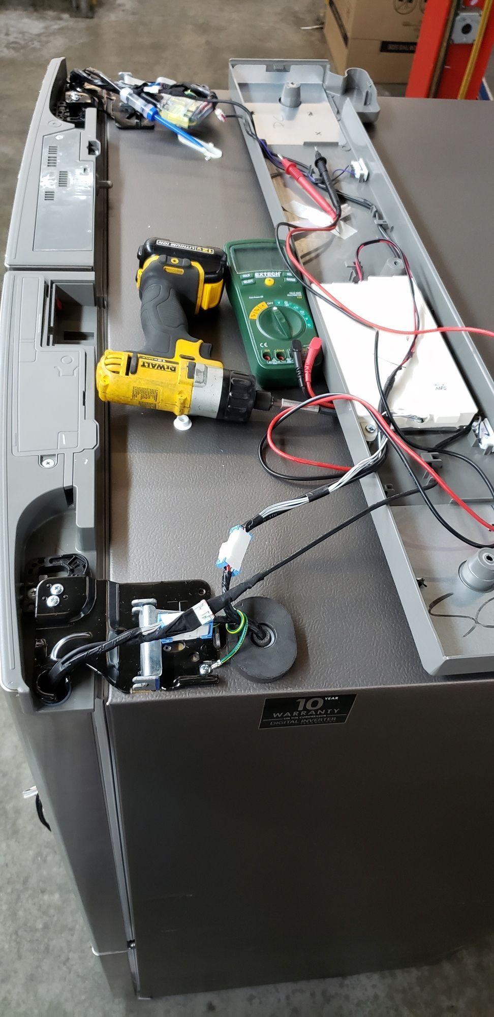 A drill and a multimeter are sitting on top of a refrigerator.