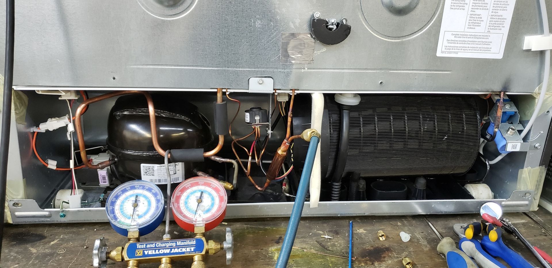 A refrigerator is being repaired with tools and gauges.