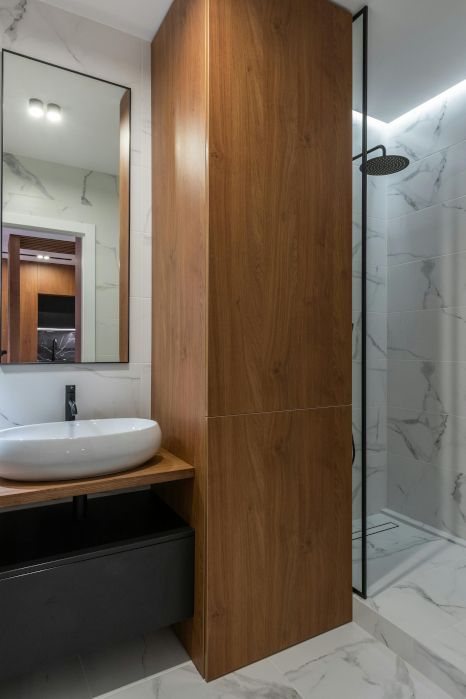 A bathroom with a sink , mirror and shower, with marble floor and wall tiling.