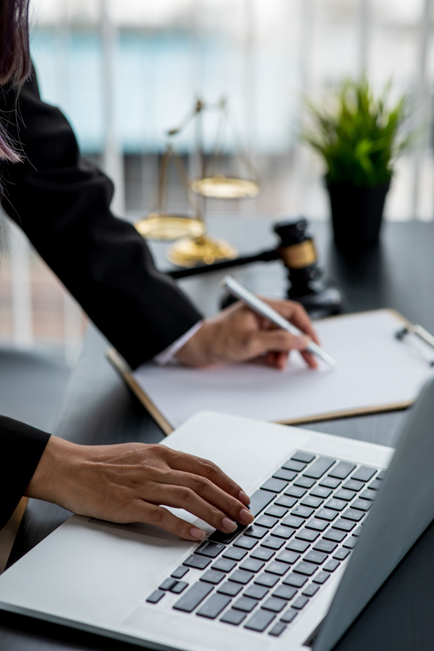 a woman is typing on a laptop in front of a scale of justice