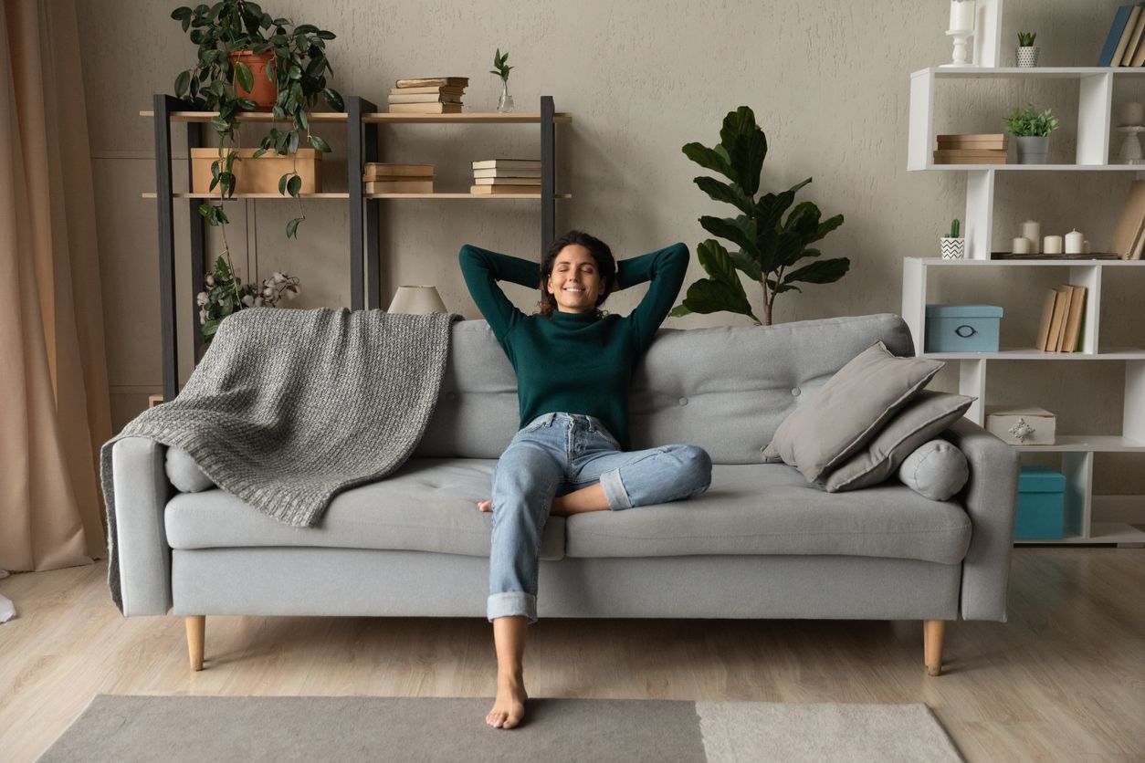 a woman sits on a couch with her hands behind her head