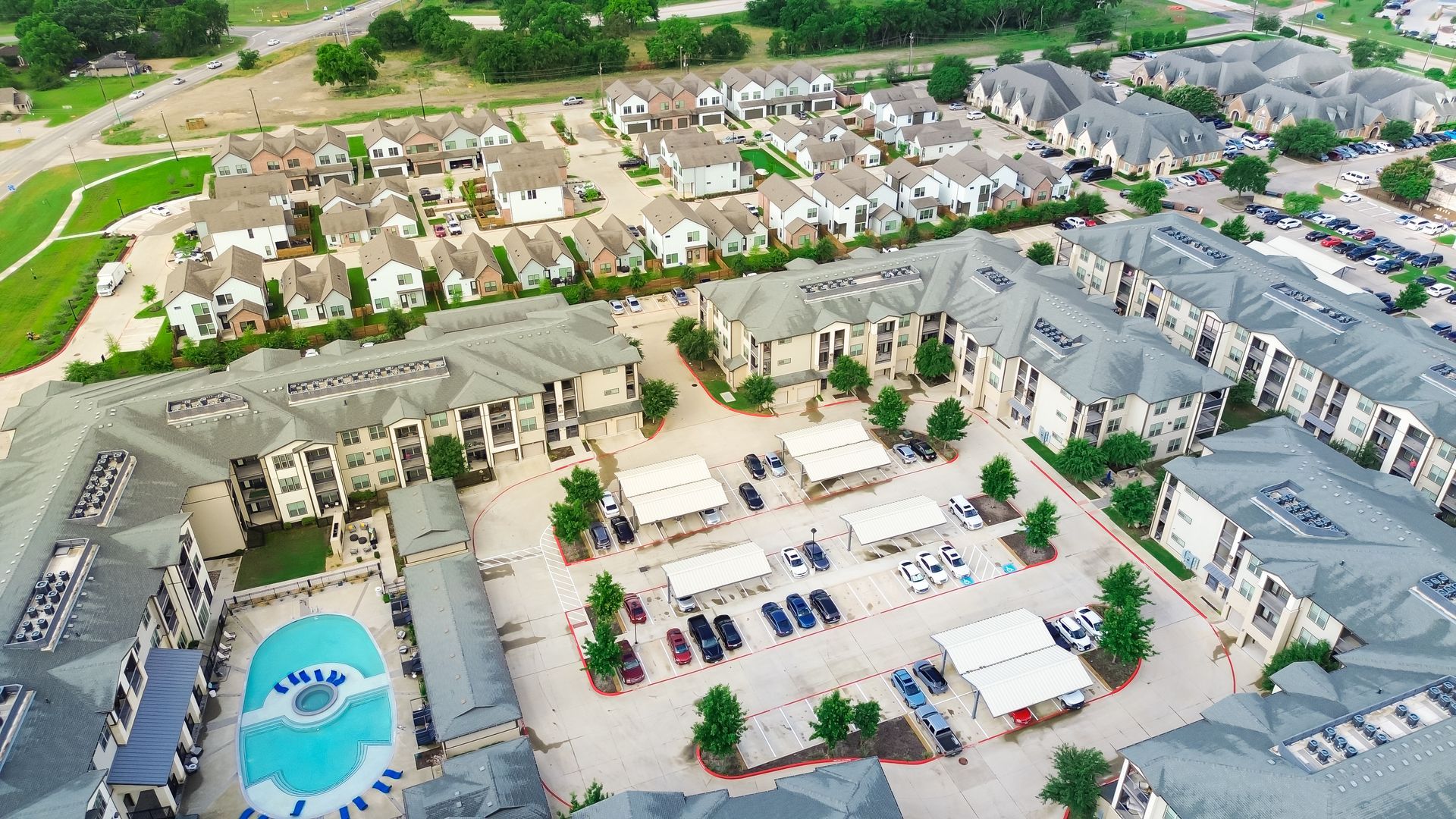 Aerial view of apartment complex with pool and townhouses, light-colored buildings.