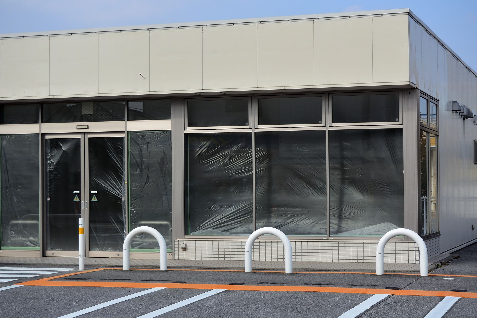 Closed storefront with boarded-up windows and metal barriers in front, under a clear sky.