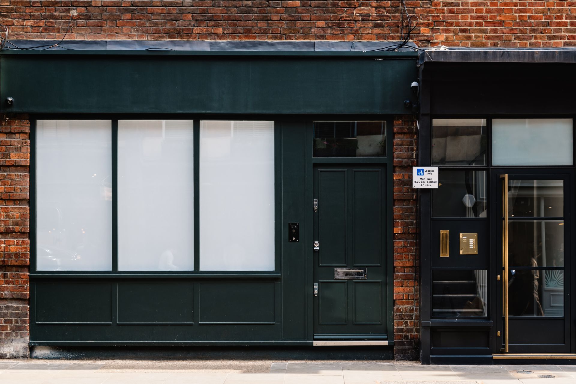Dark green storefront with white-covered windows and door next to a black doorway, all against a brick wall.