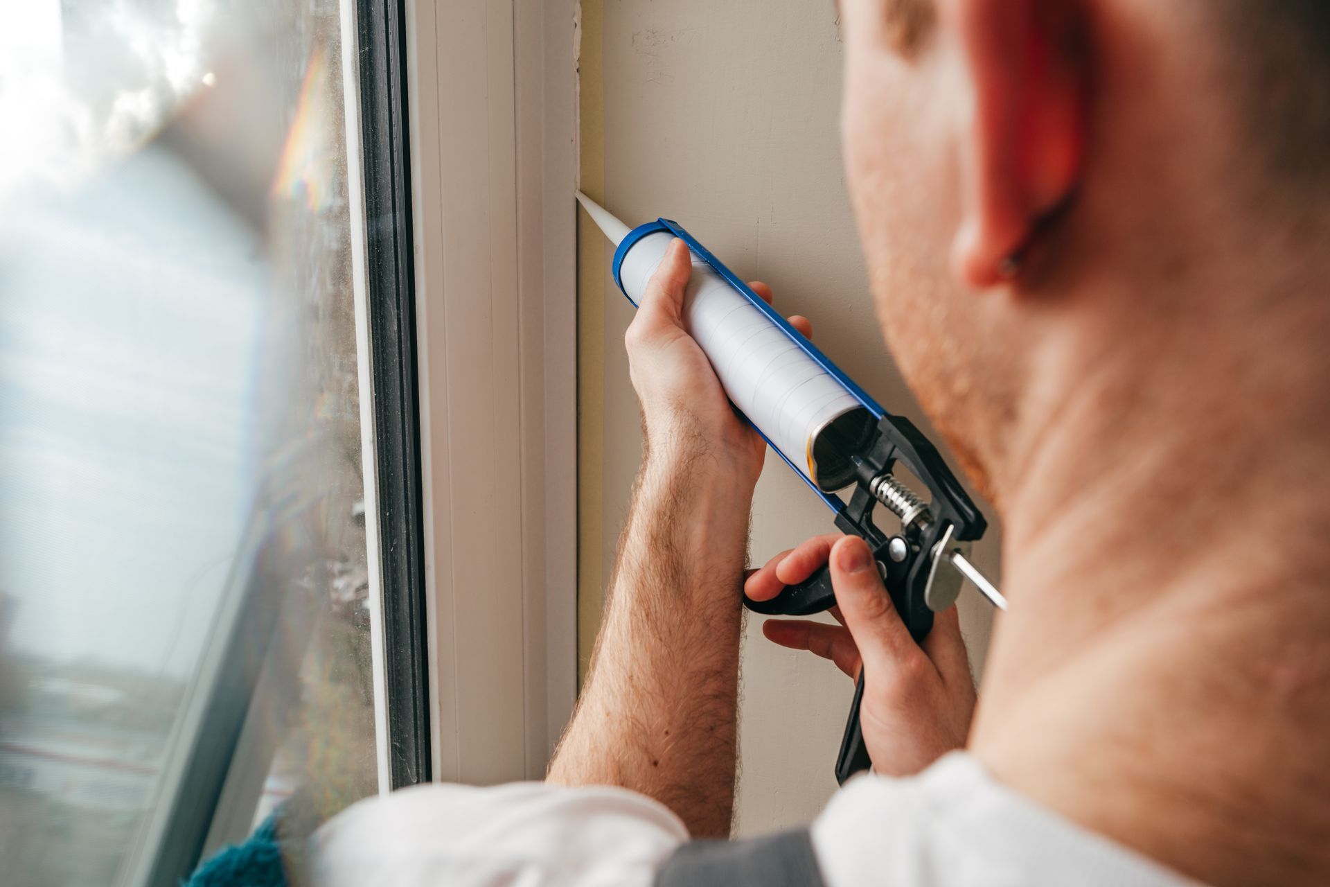 Person applying sealant to a window frame with a caulk gun.