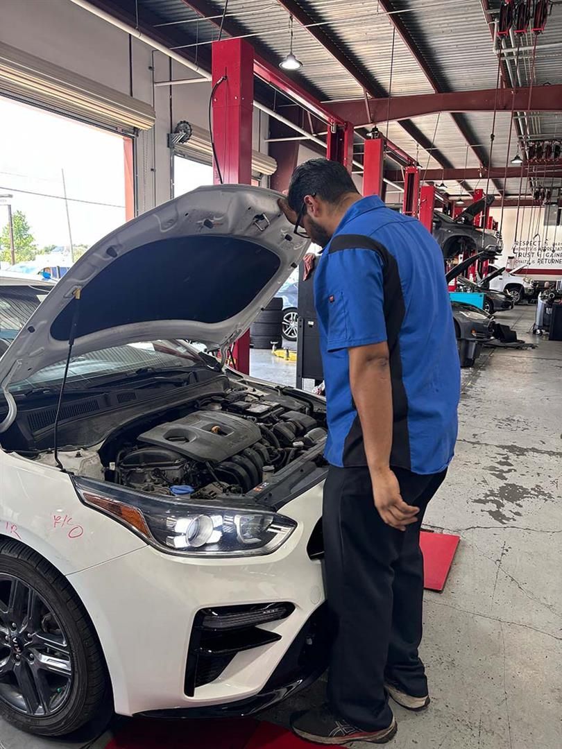 A man is looking under the hood of a car in a garage. | Elite Auto Experts