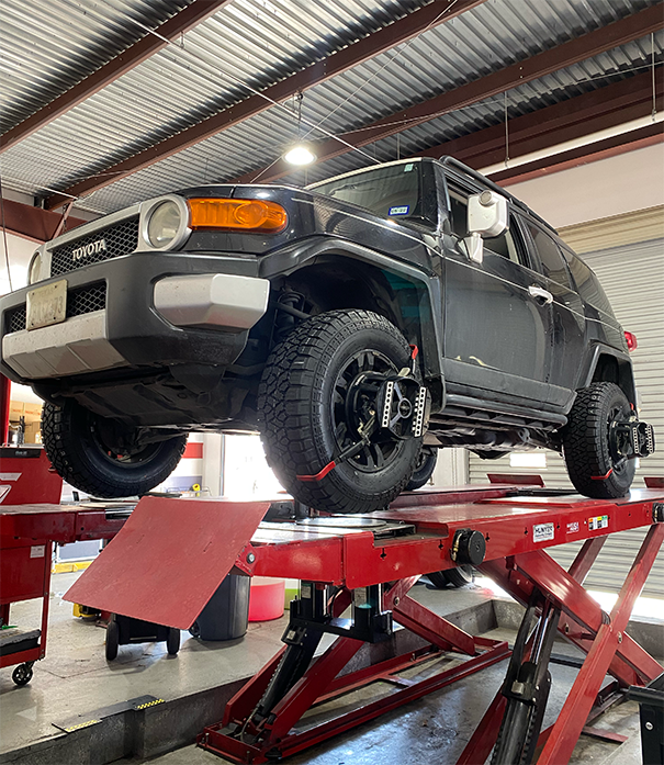 A black suv is sitting on top of a red lift in a garage. | Elite Auto Experts