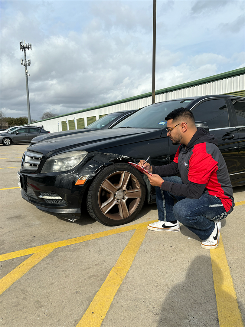 A man is kneeling down next to a car in a parking lot. | Elite Auto Experts