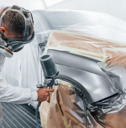 A man is spray painting a car fender in a garage. | Elite Auto Experts
