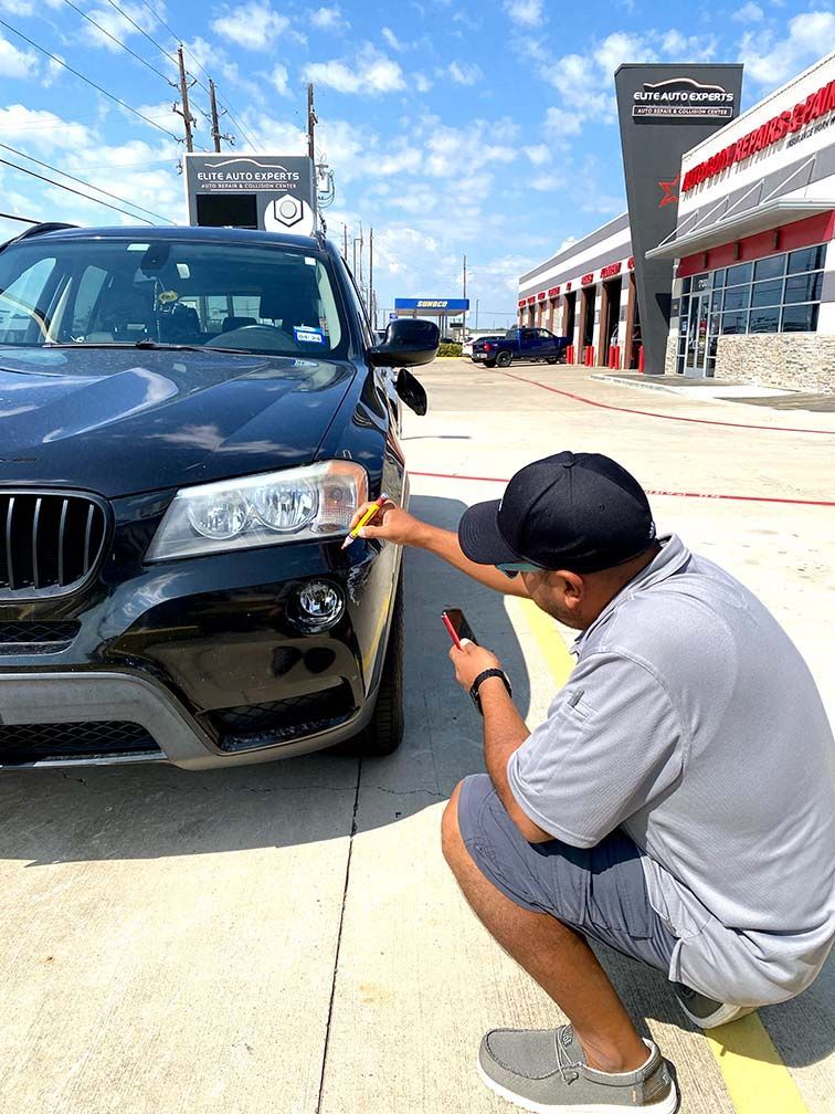 A man is kneeling down in front of a bmw x3 and looking at his phone. | Elite Auto Experts