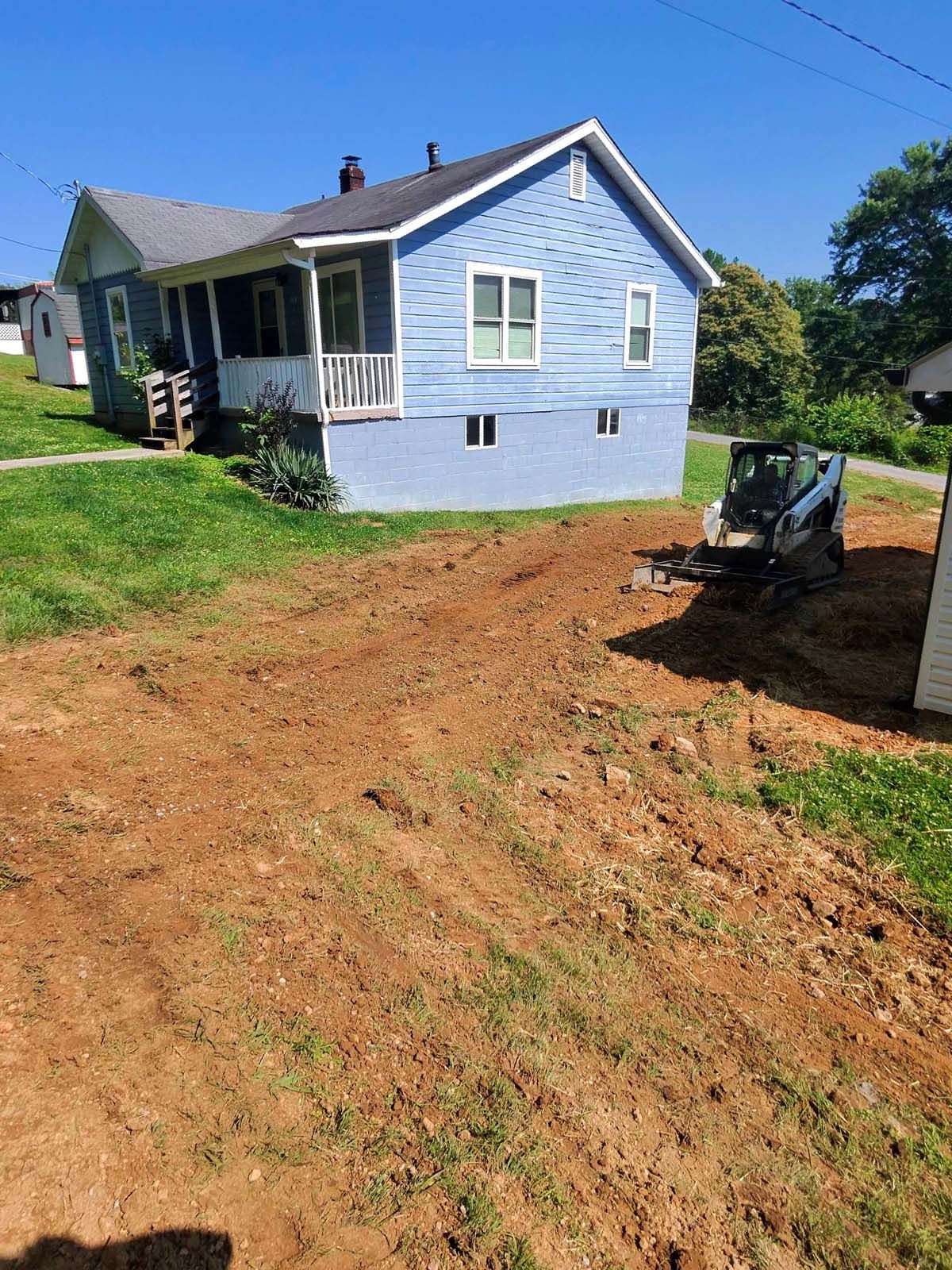A blue house is sitting on top of a hill next to a dirt road.