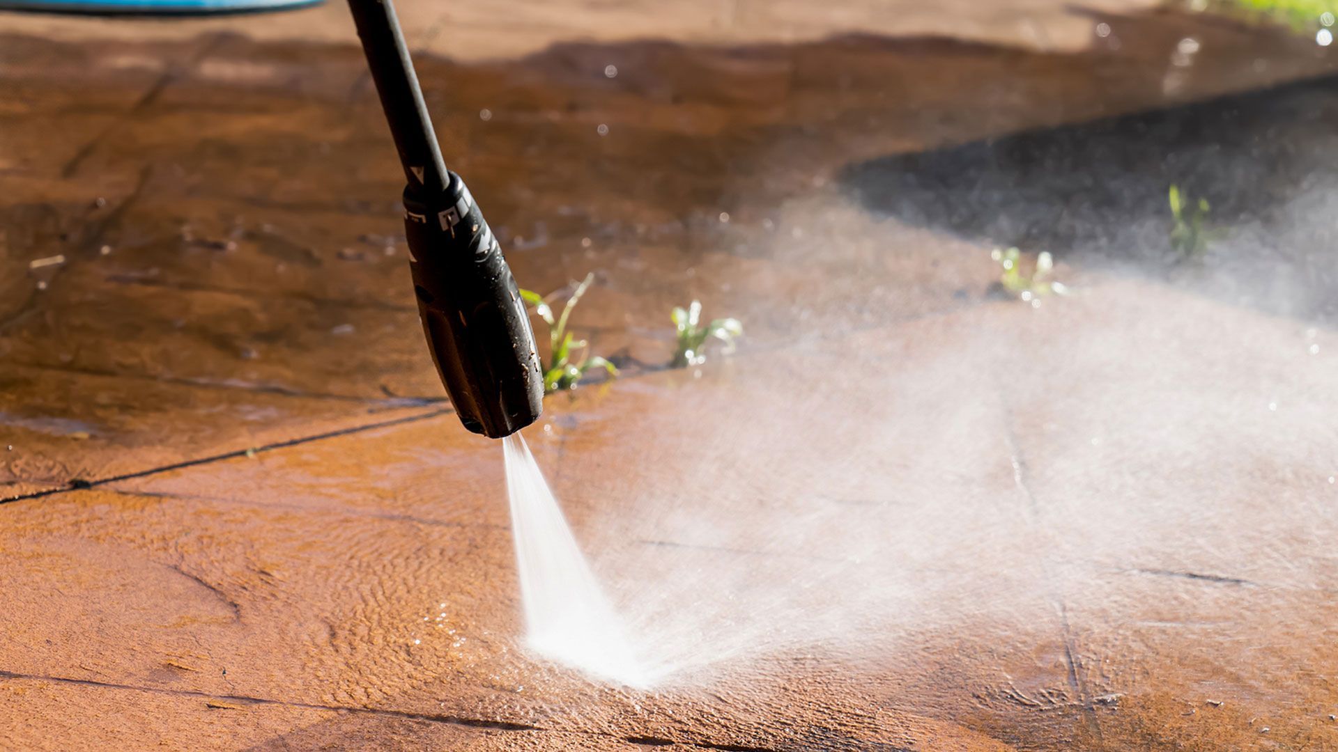 A person is using a high pressure washer to clean a sidewalk.