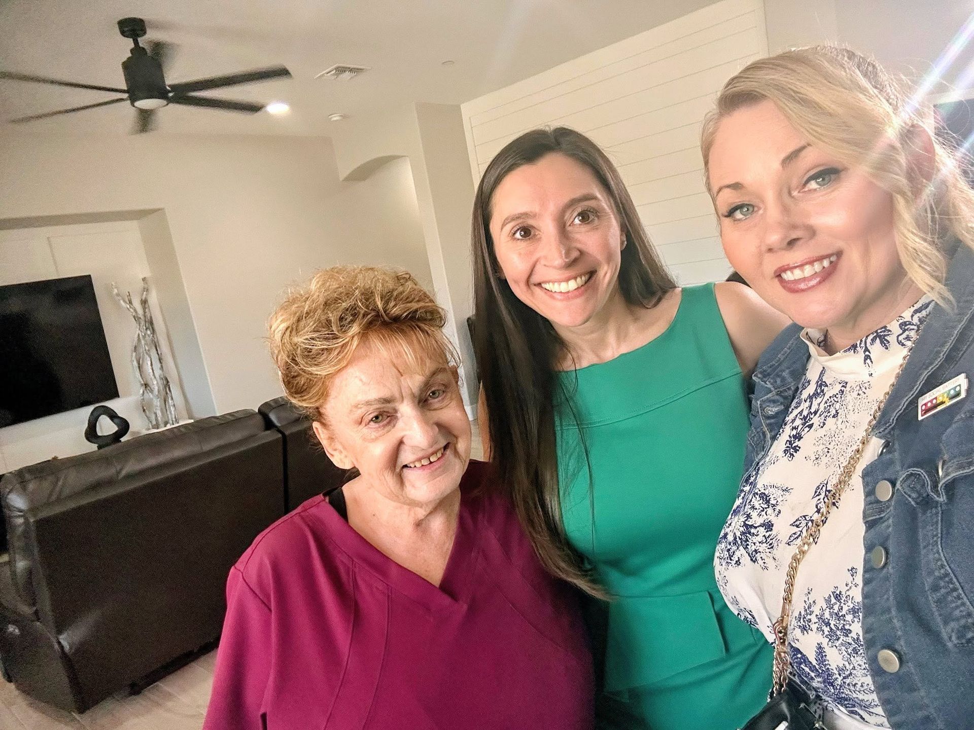 Three women smiling in a living room, one holding the camera for a selfie.