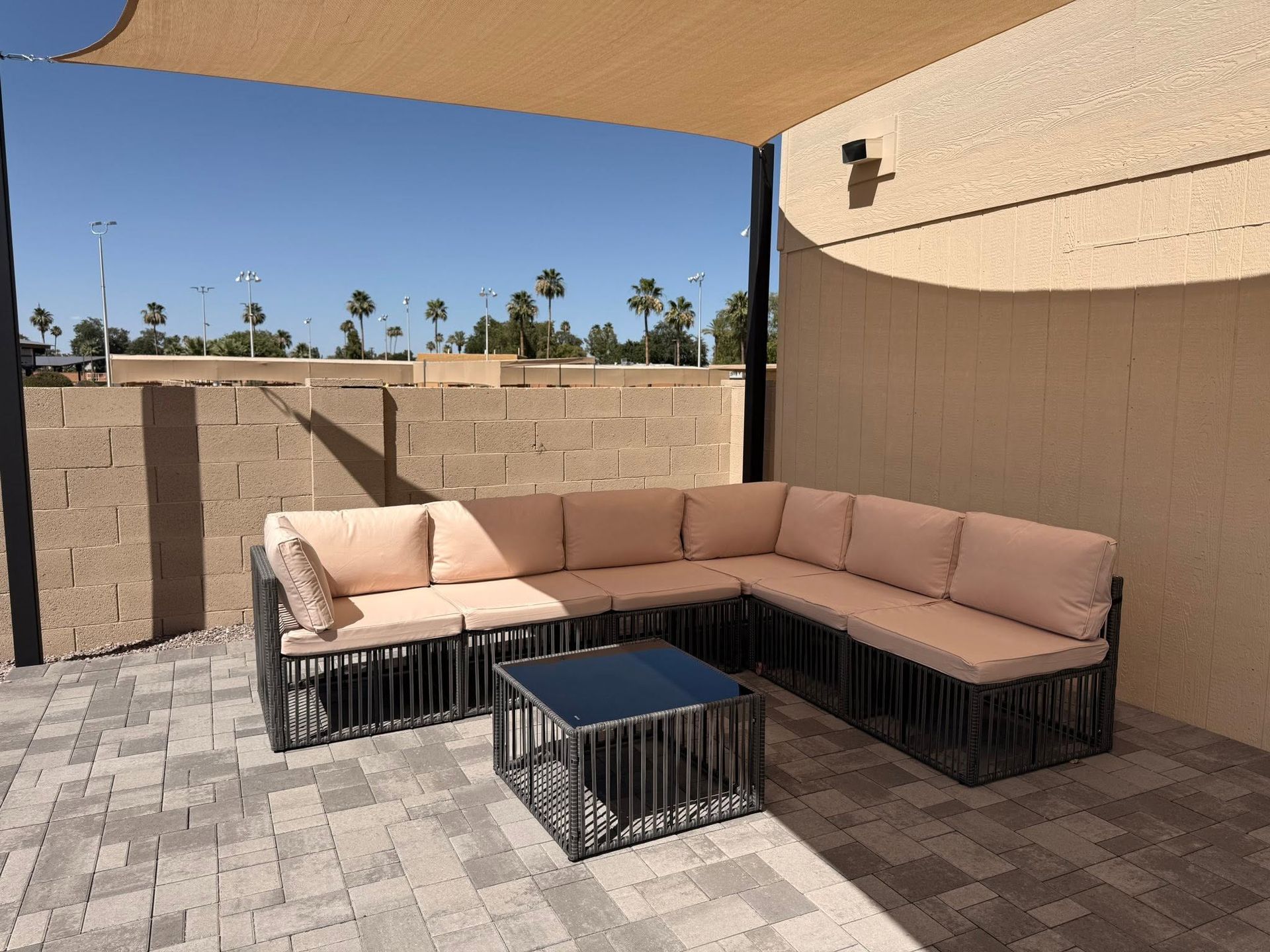 Beige sectional sofa with coffee table on a shaded patio, overlooking a desert-style yard with palm trees.