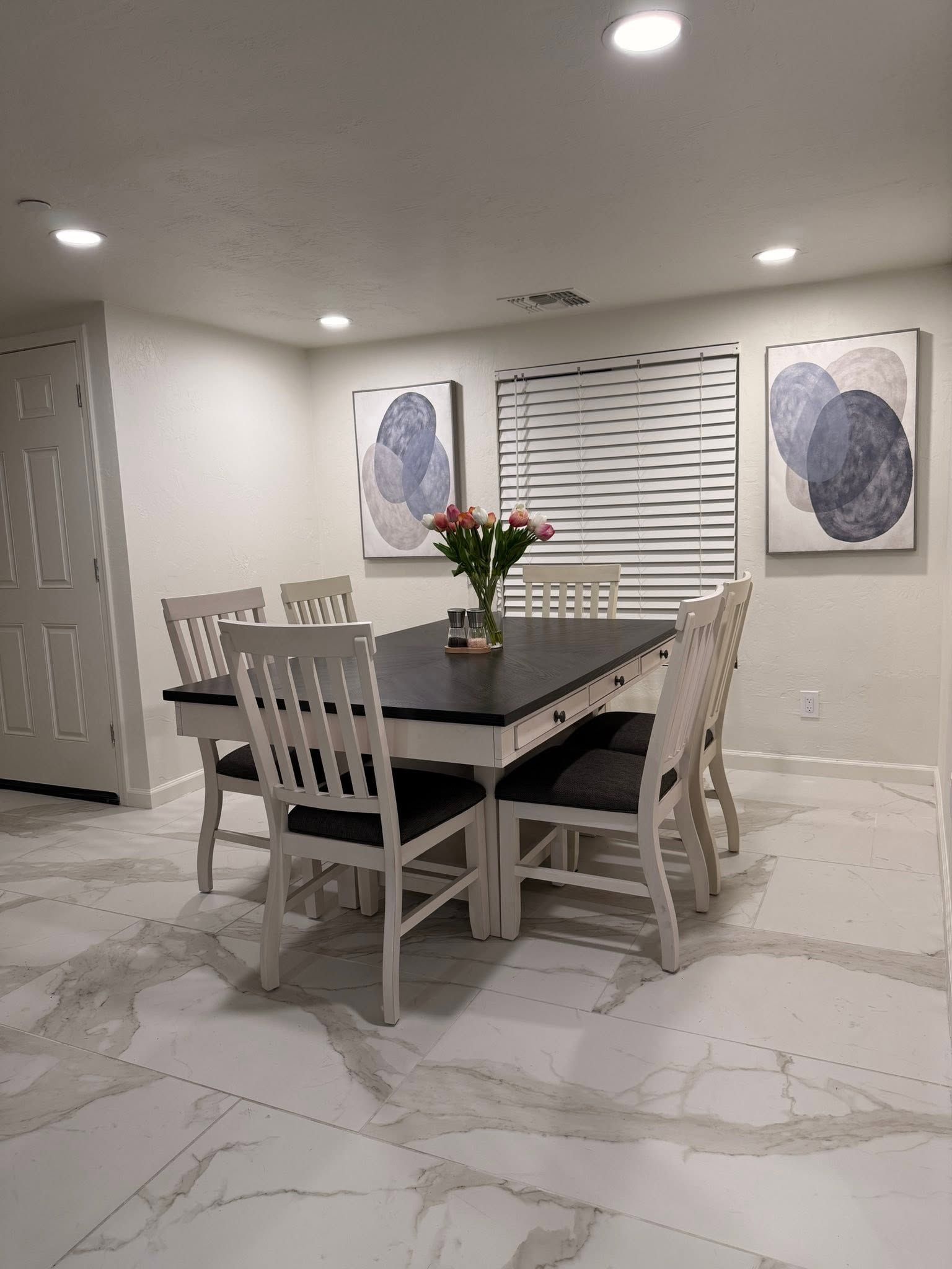 Modern dining room with a black table, white chairs, floral centerpiece, and abstract wall art.