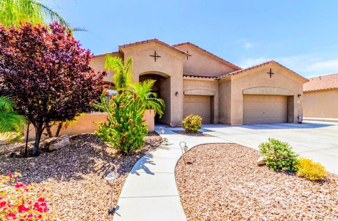 Single-story stucco house with a two-car garage, curved walkway, and desert landscaping under a blue sky