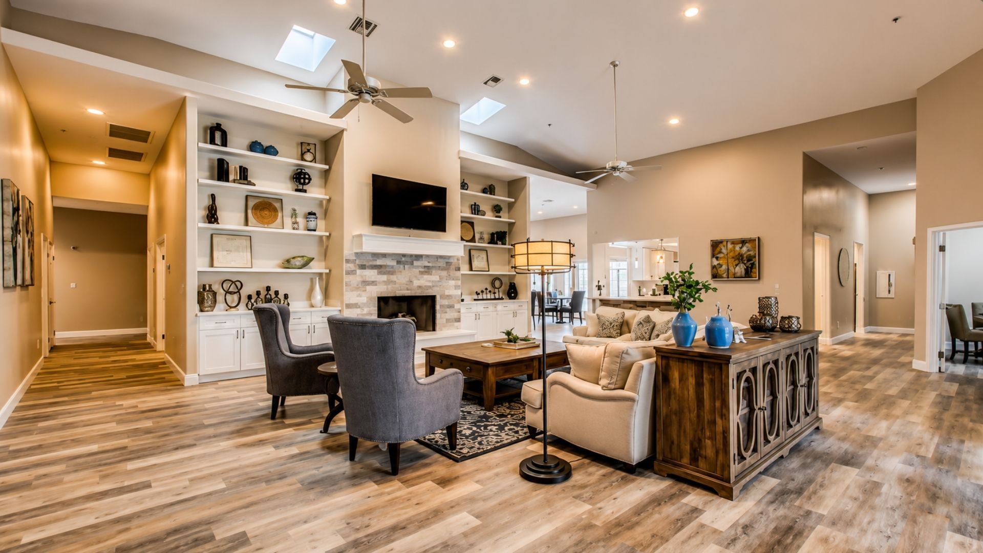 Open-concept living room with fireplace, TV, dining table, and hardwood floors in warm neutral tones