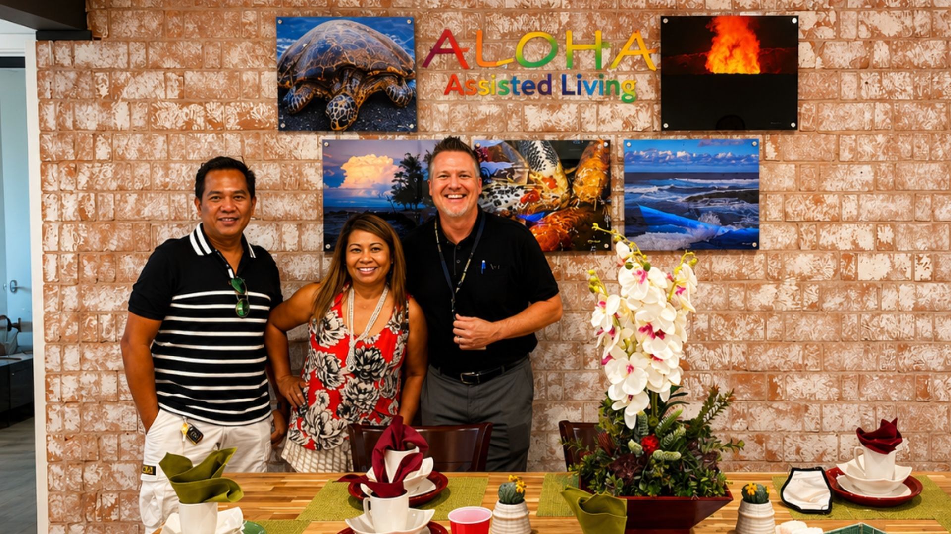 Three people smiling behind a decorated table in front of a wall of scenic travel photos.
