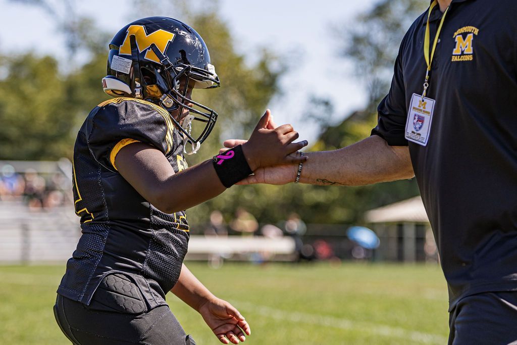 Football player in maroon jersey holding ball, smiling, surrounded by teammates on a field.