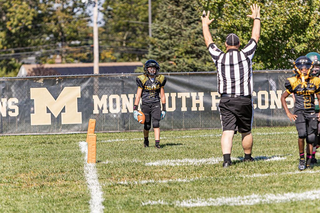 Football players in action on a grassy field; one runs with the ball, pursued by two opponents.