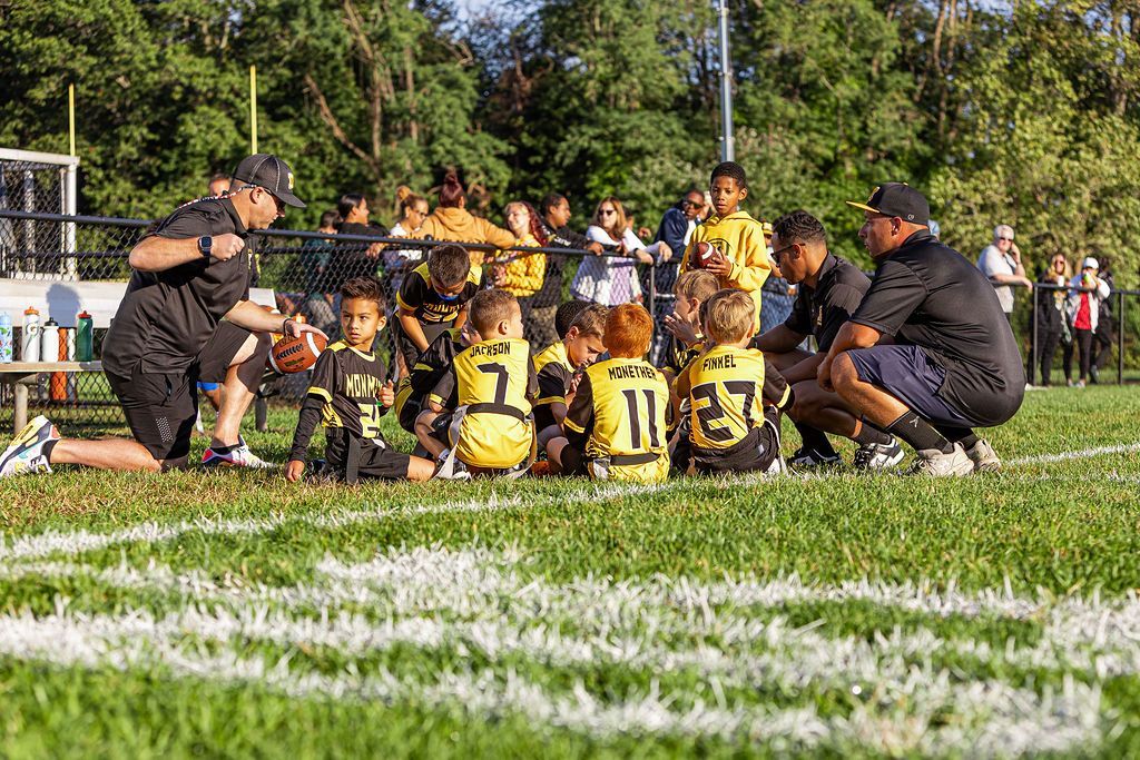 Football players huddle around a football, reaching hands together, blue sky backdrop.