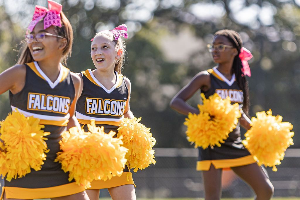 Cheerleader in red uniform performs a backbend on a green and red football field.