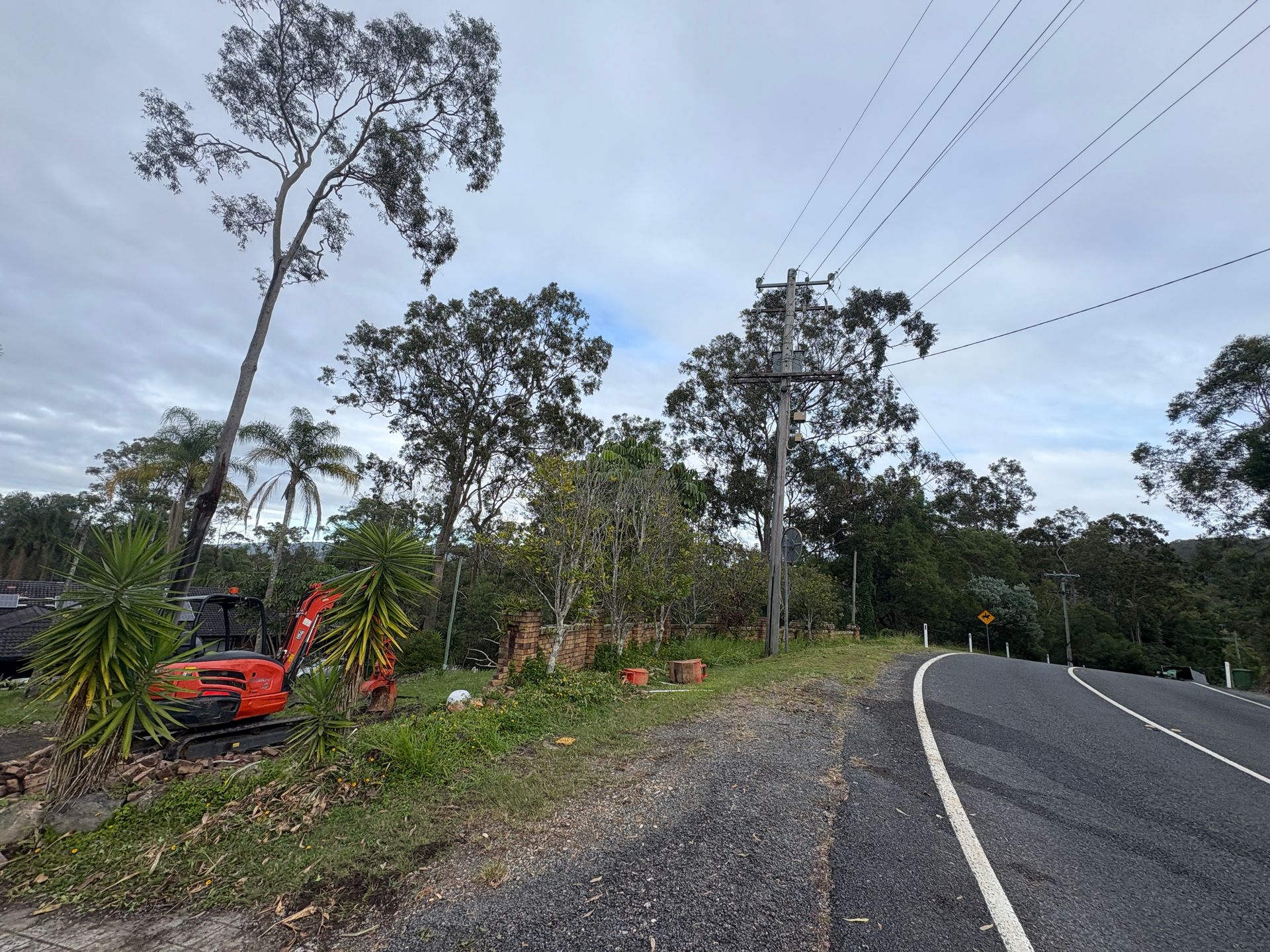 A red excavator is parked on the side of the road next to a road.