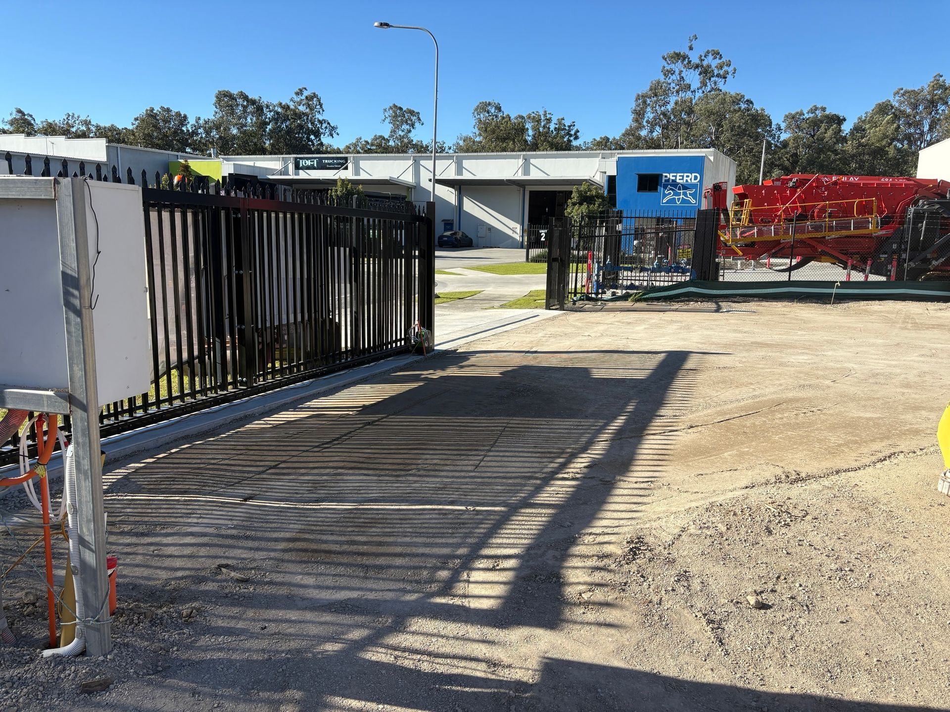 A fence surrounds a dirt area with a building in the background
