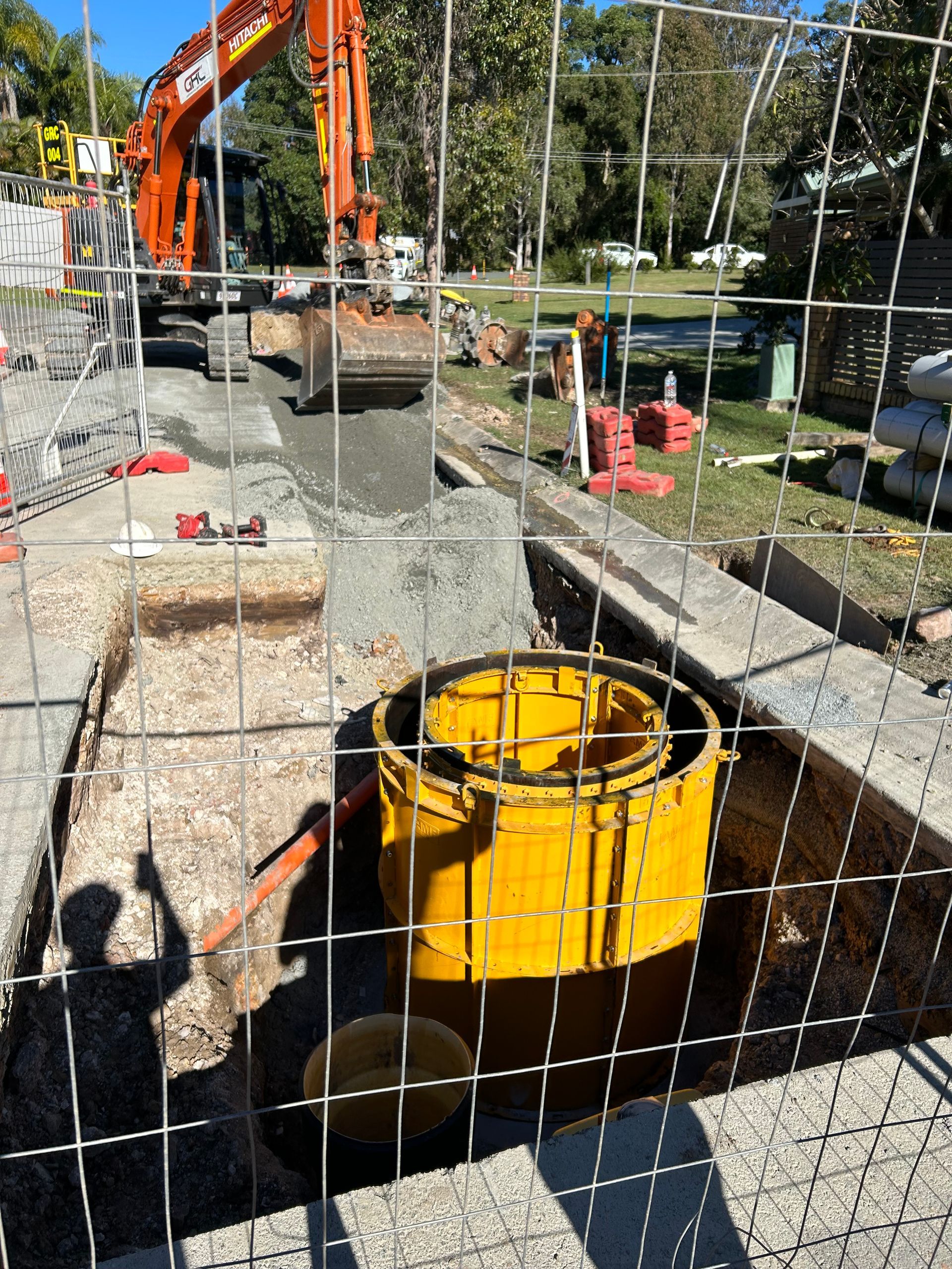 A yellow bucket is sitting in a hole in the ground behind a fence.