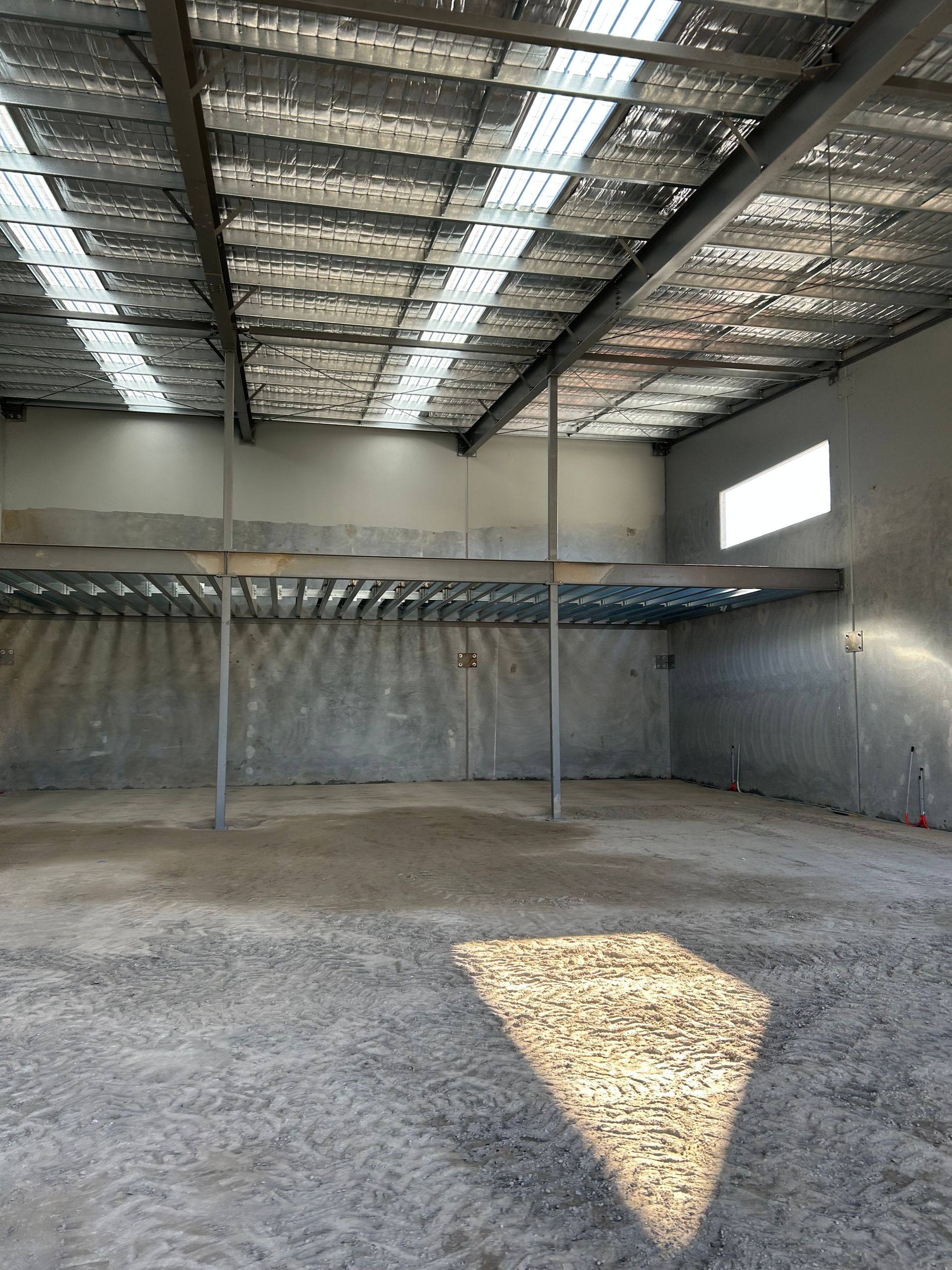 An empty warehouse with a metal roof and a shadow on the floor.