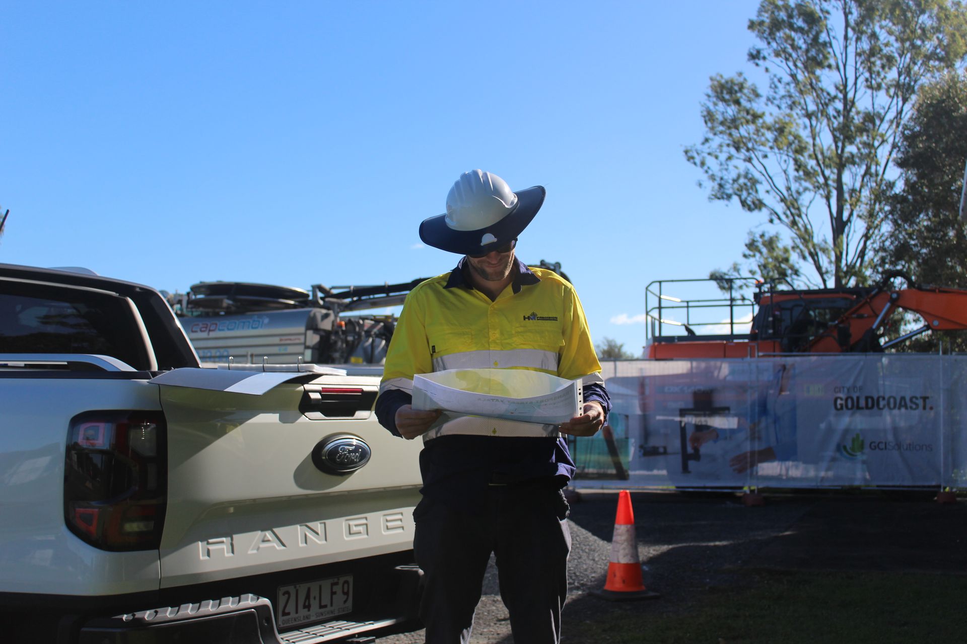 A man in a hard hat is standing in front of a range rover holding a piece of paper.