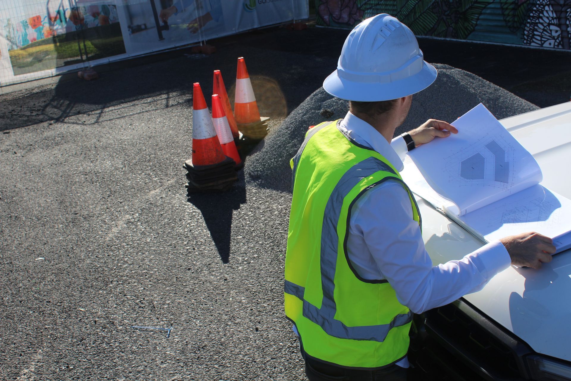 A man wearing a hard hat and safety vest is looking at a blueprint.