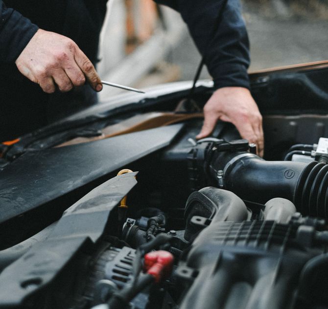 Hands working with a screwdriver on a car engine in an open hood compartment