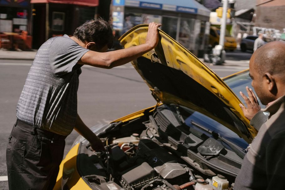 Man opening the hood of a yellow car on a city street, with another person standing nearby