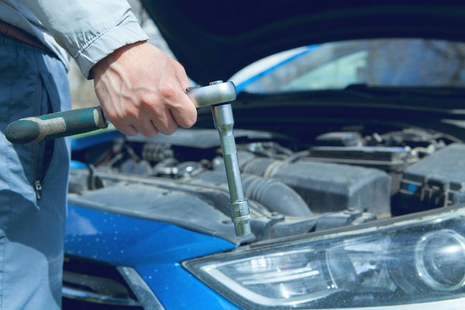 Mechanic using a ratchet wrench on a blue car with the hood open