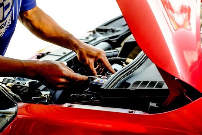 Mechanic working under a red car hood, inspecting the engine compartment