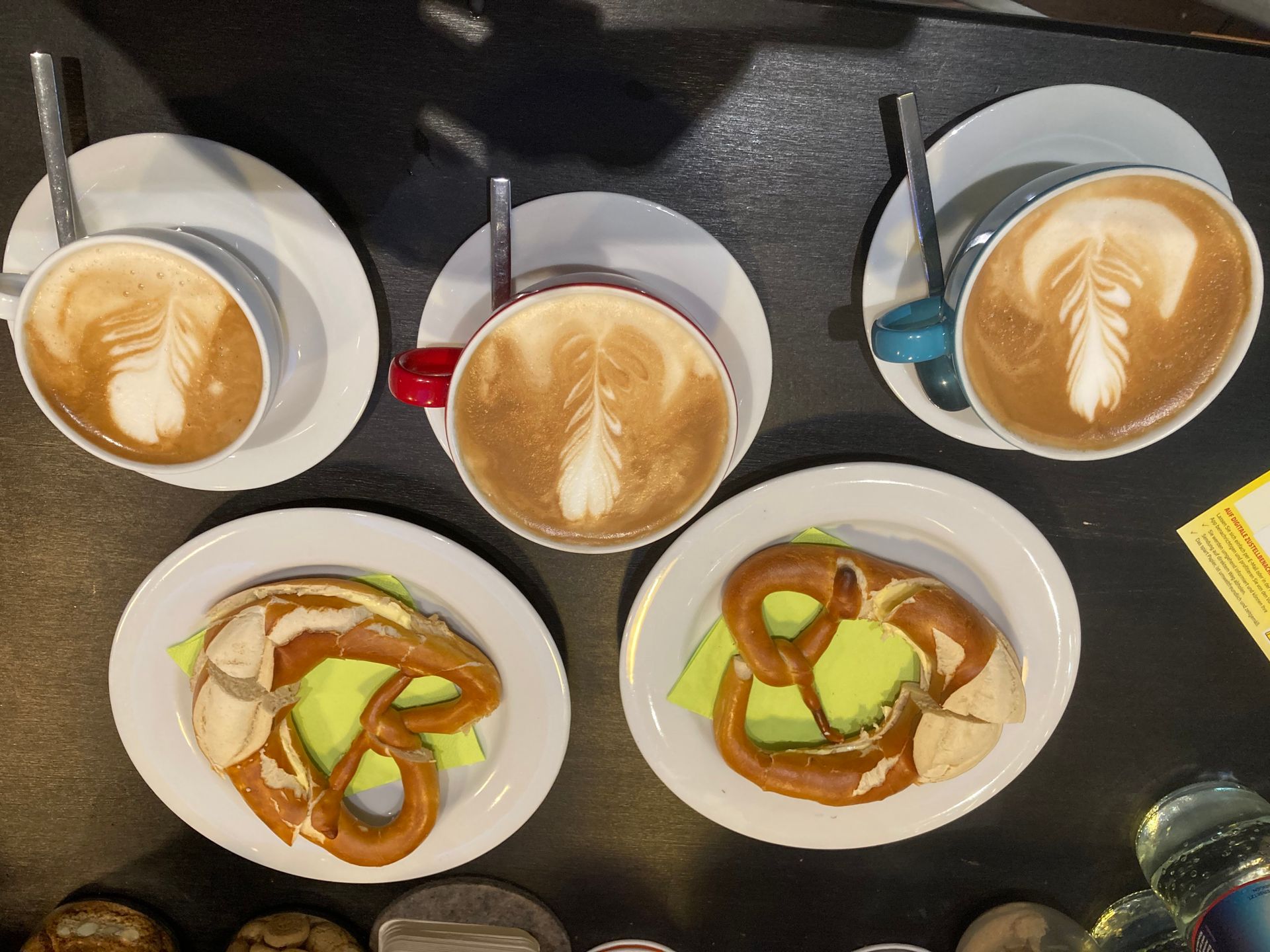 Vier Tassen Kaffee und zwei Teller mit Brezeln auf einem Tisch