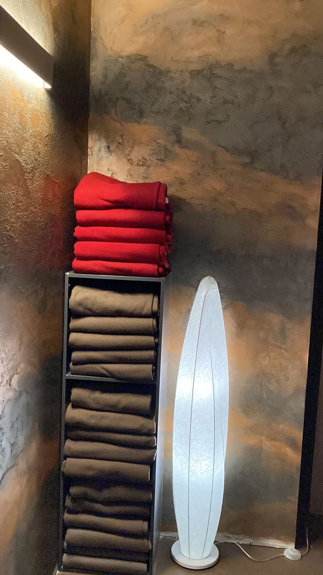 Ein Stapel Handtücher liegt auf einem Regal neben einer Lampe.