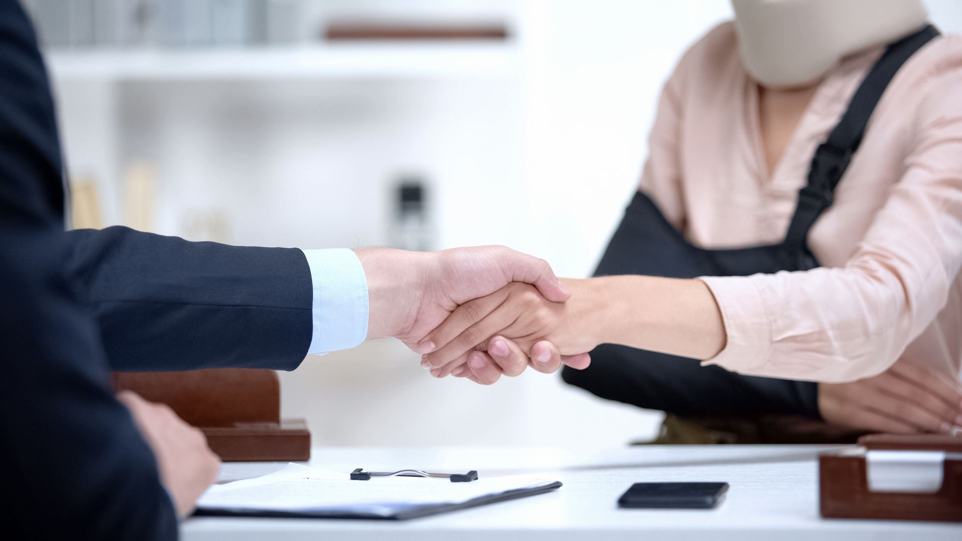 Personal injury lawyer shaking hands with client wearing neck brace and arm sling.