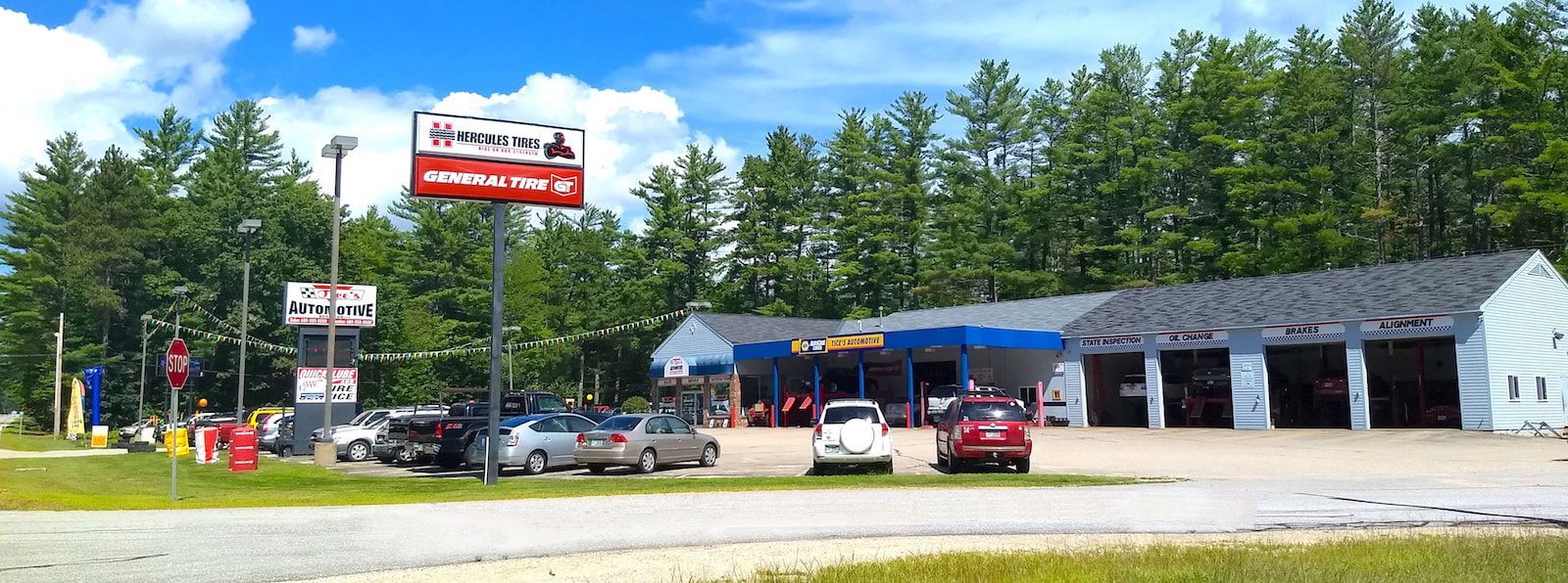 An automotive service center with multiple garage bays, a parking lot, and business signage under a blue sky.