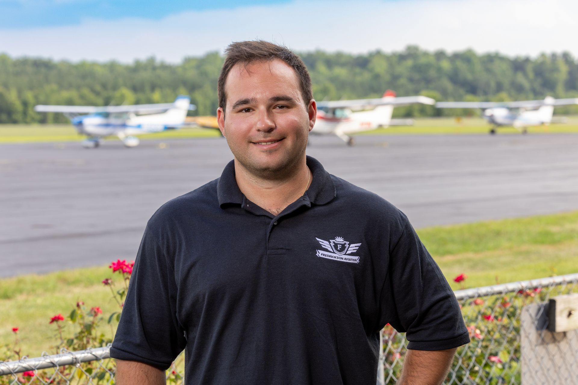 A man is standing in front of a runway with planes in the background.