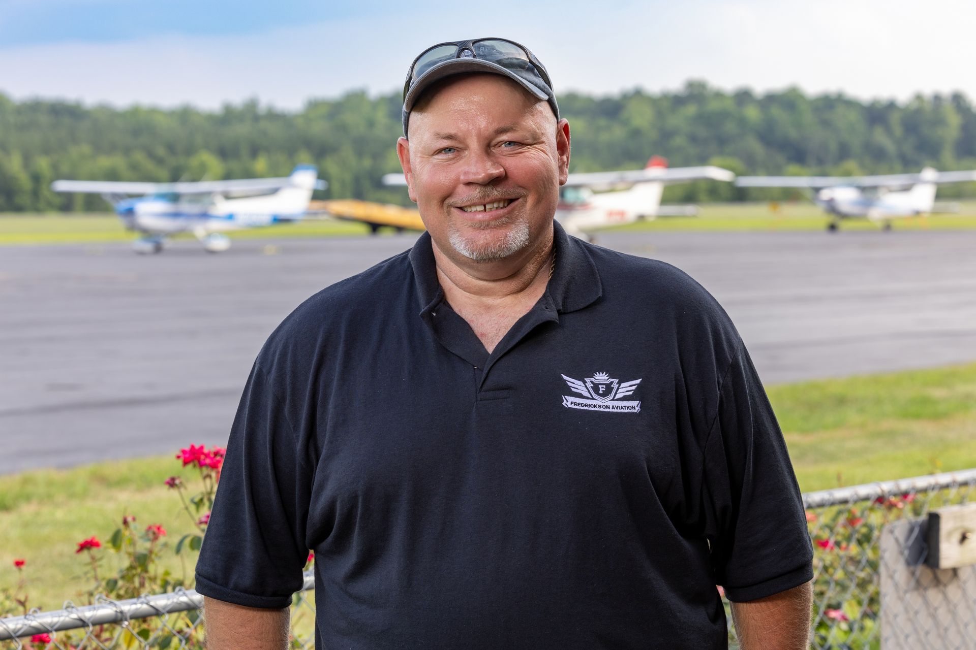 A man is standing in front of a runway with planes in the background.