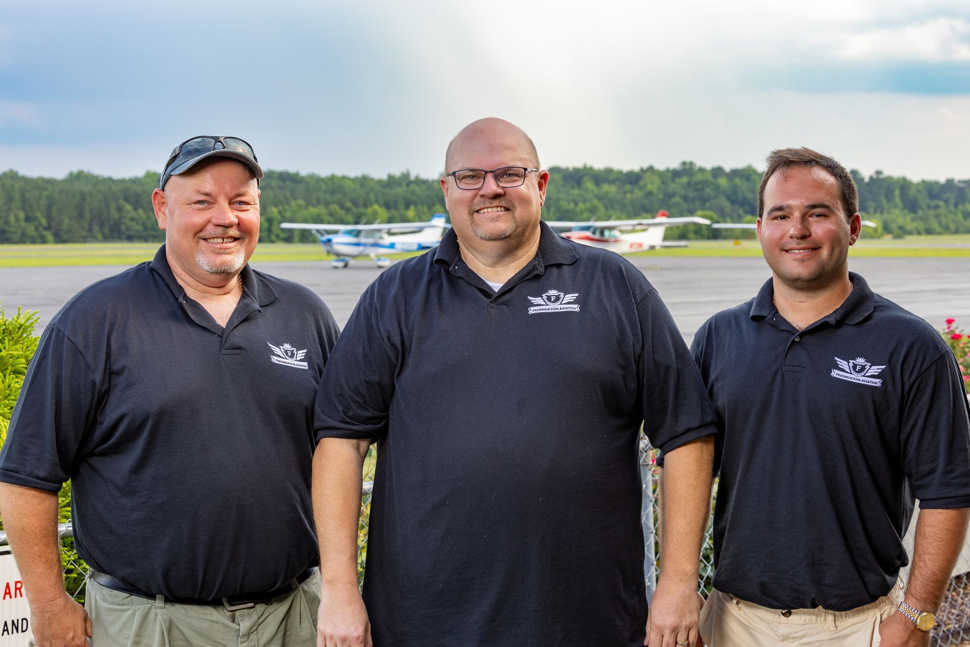 Three men are standing next to each other on a runway with a plane in the background.