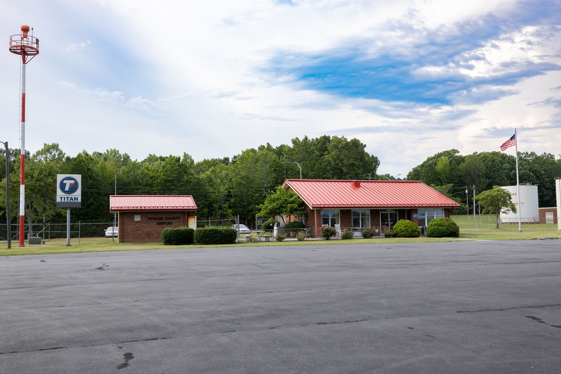 A small building with a red roof is in the middle of a parking lot.