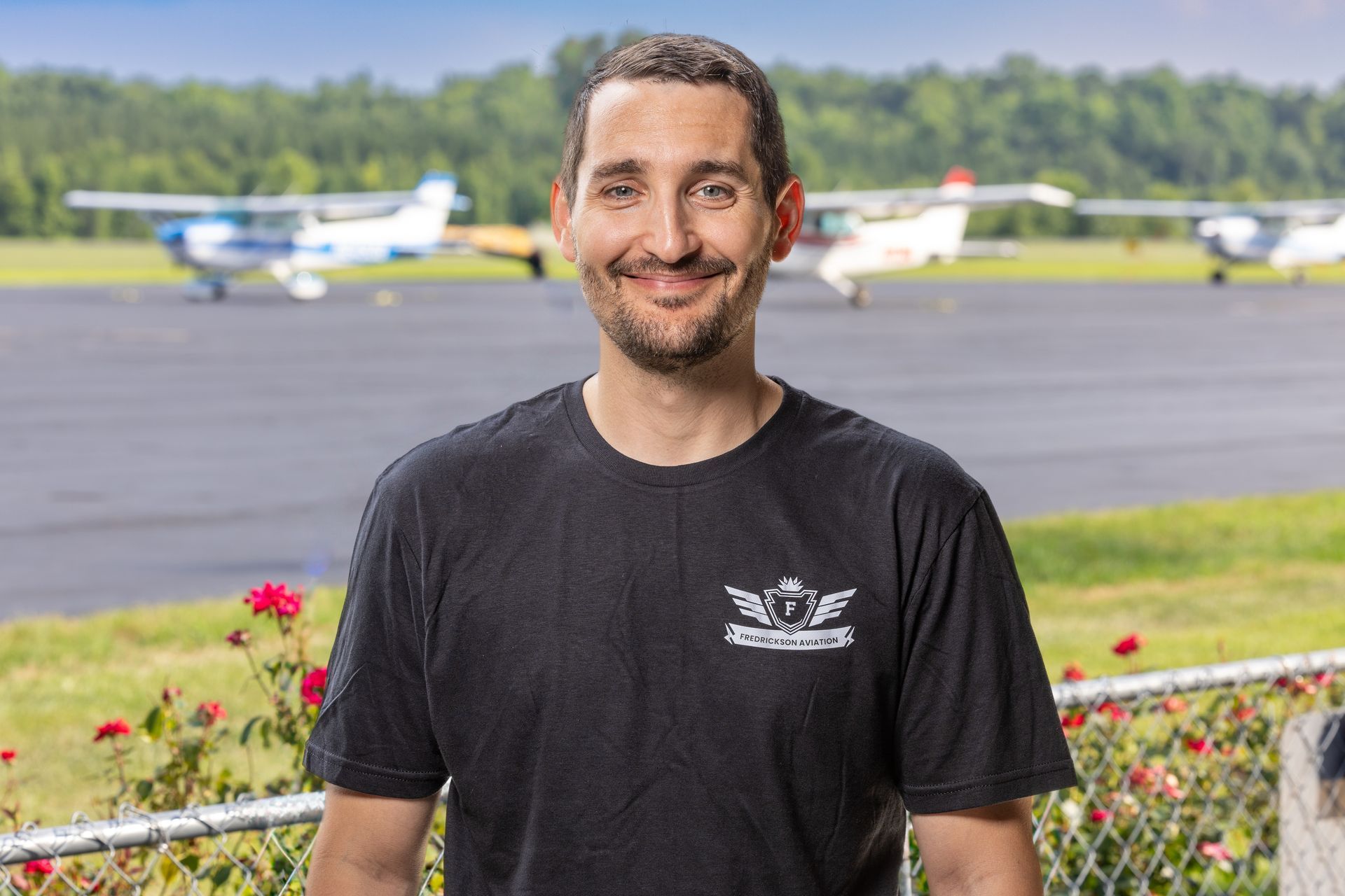 A man in a black shirt is standing in front of a runway with planes in the background.